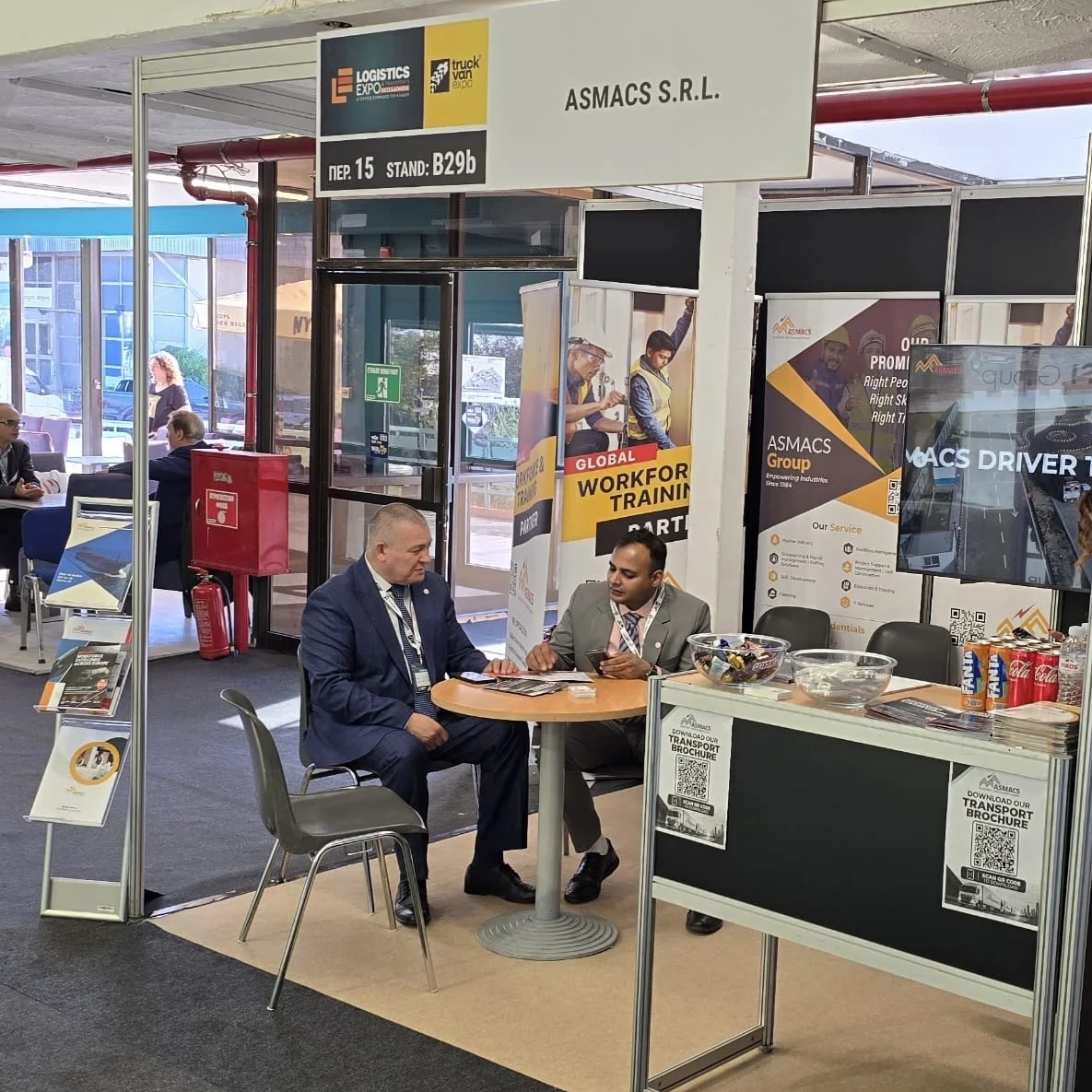 ASMACS S.R.L. stand B29b at Logistics Expo 2026, Thessaloniki, Greece, with the ASMACS team meeting a visitor